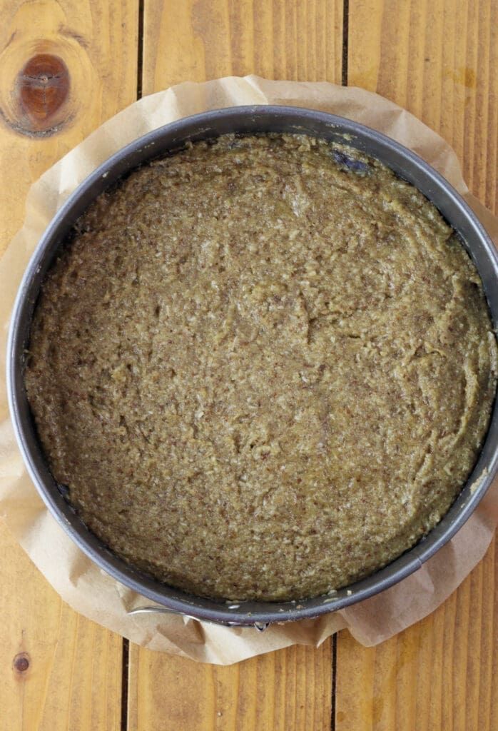 Adding the cake batter on the plum halves in a round cake baking pan.
